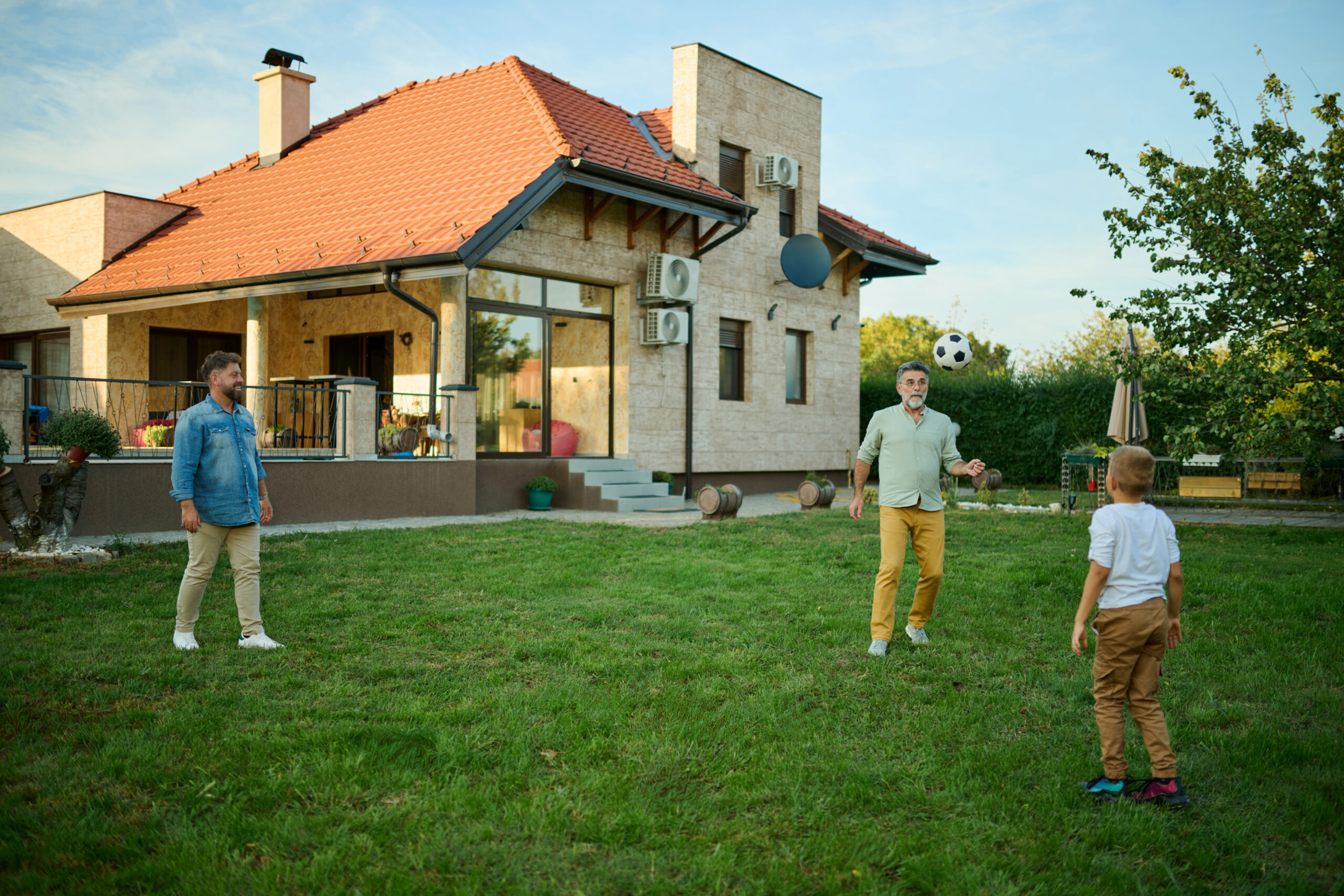 Three generations playing football in their backyard on a sunny day, bonding over a game of catch