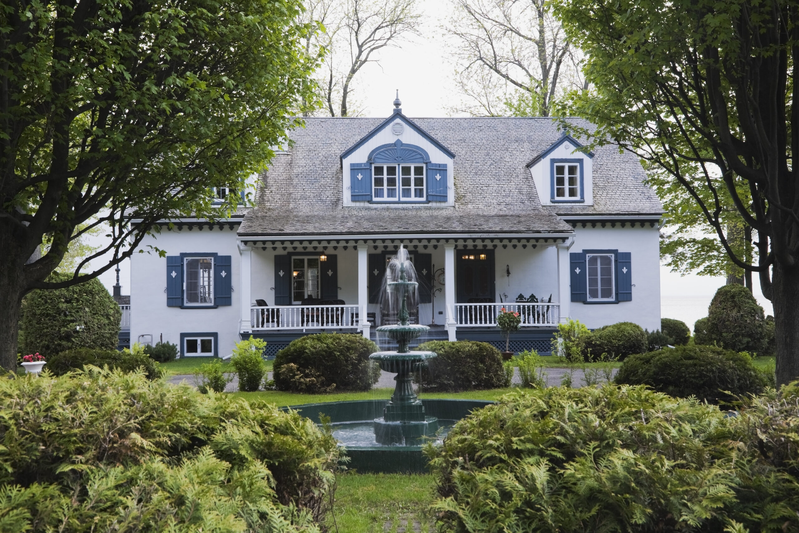 White with blue trim 1920s cottage style house facade with water fountain, Quebec, Canada